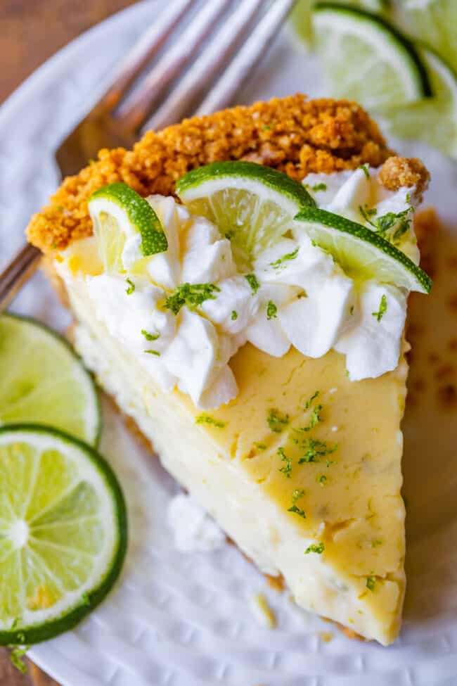 a slice of key lime with with a graham cracker crust, whipped cream, and lime slices.