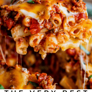 A close-up of a cheesy baked ziti slice being lifted, with gooey melted cheese stretching and visible layers of pasta, hearty meat sauce, and herbs. Text at the bottom reads: The Very Best Cheesy Baked Ziti of Your Life.