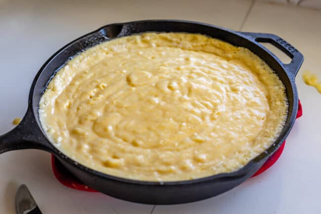 cornbread batter bubbling and cooking on the edges in a preheated cast iron skillet.