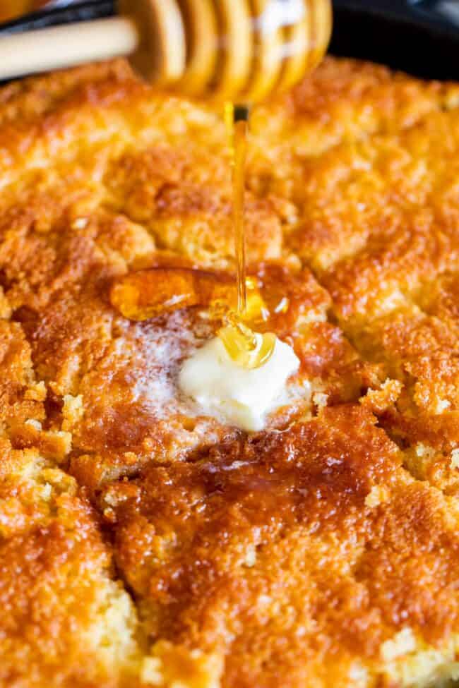 cornbread sliced in the cast iron pan, topped with melting butter and being drizzled with honey.