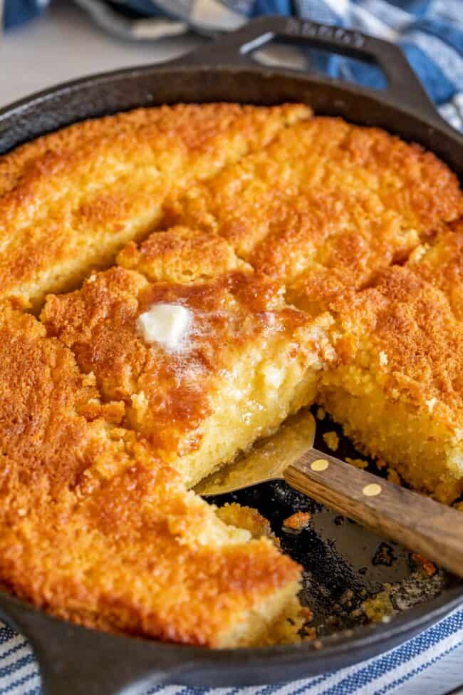 cornbread with butter melting on top, sliced in a skillet, a spatula lifting the center piece.