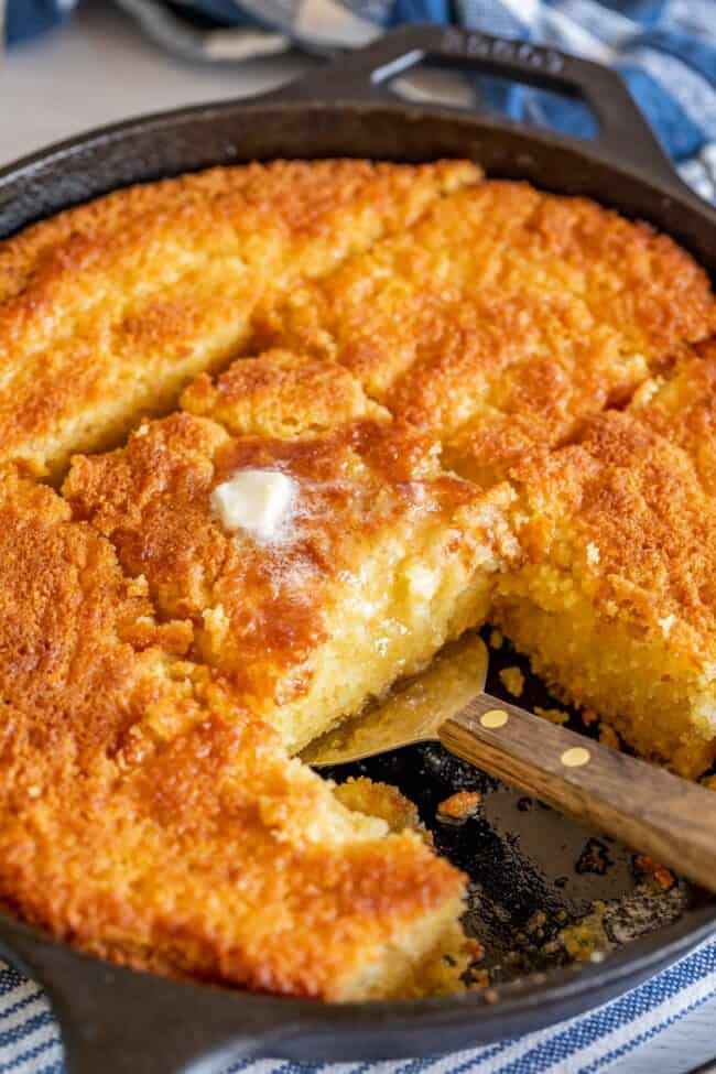 sweet cornbread sliced in a skillet, spatula lifting center piece