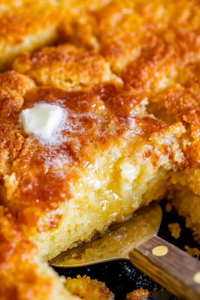 cornbread being lifted from a pan with a spatula, topped with a pat of butter melting.