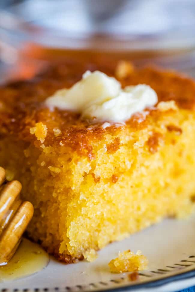 a piece of cornbread on a plate topped with butter and honey on the side.