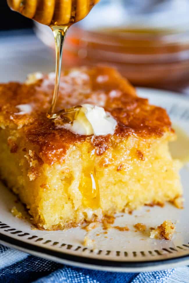 cornbread being drizzled with honey, on a plate, with a pat of butter melting on top. 
