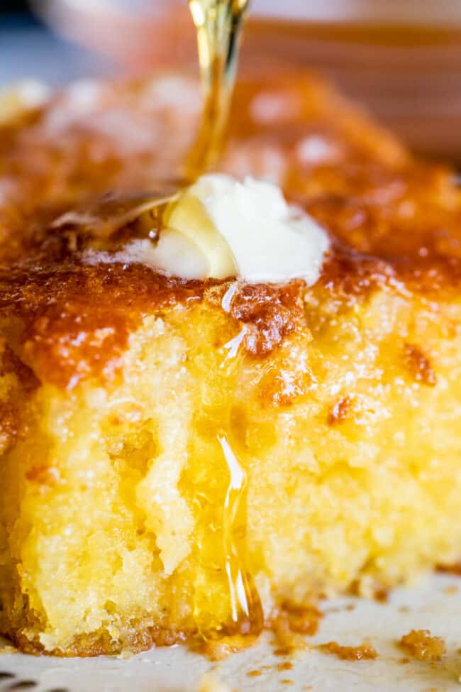 cornbread on a plate, shot close up, topped with melting butter and drizzled with honey.