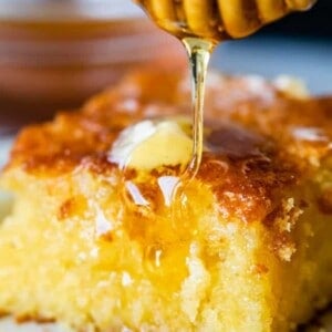 A close-up of a piece of cornbread with a pat of melting butter on top, as honey from a honey dipper drizzles over it, capturing the essence of a delicious cornbread recipe.