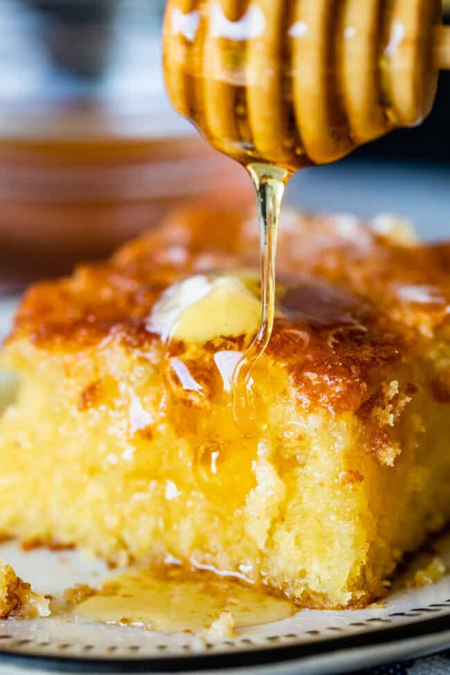 cornbread on a plate with melting butter and honey being drizzled on top. 
