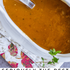 A white gravy boat filled with rich brown turkey gravy, garnished with fresh herbs, sits on a floral napkin. Text below reads, Seriously classic turkey gravy. The Food Charlatan.
