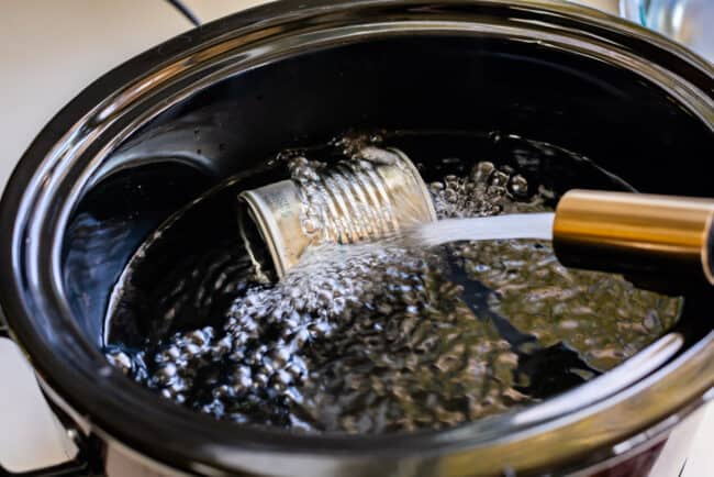 adding water to a crockpot with a can of sweetened condensed milk for making dulce de leche.