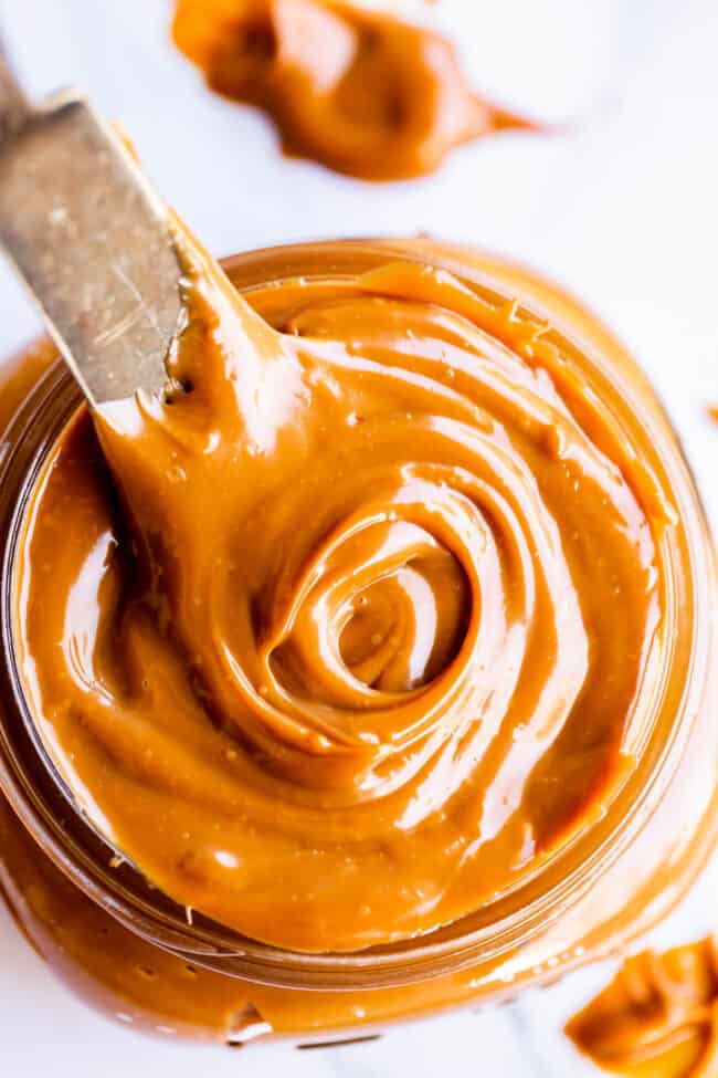 dulce de leche in a glass jar being swirled with a knife.