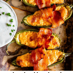 A tray of halved jalapeƱos stuffed with creamy cheese and wrapped in crispy bacon, served alongside a bowl of white dipping sauce with chopped chives. Text reads: āTruly Delicious Bacon Wrapped Jalapeno Poppers.ā.