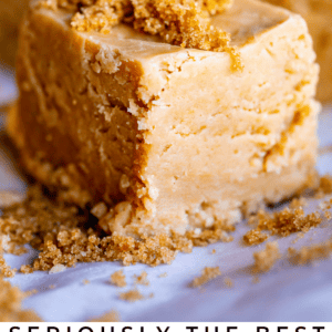 Close-up of a thick, square piece of homemade brown sugar fudge topped with loose brown sugar, with more fudge pieces in the background. Text reads: Seriously delicious penuche. Creamy brown sugar fudge.