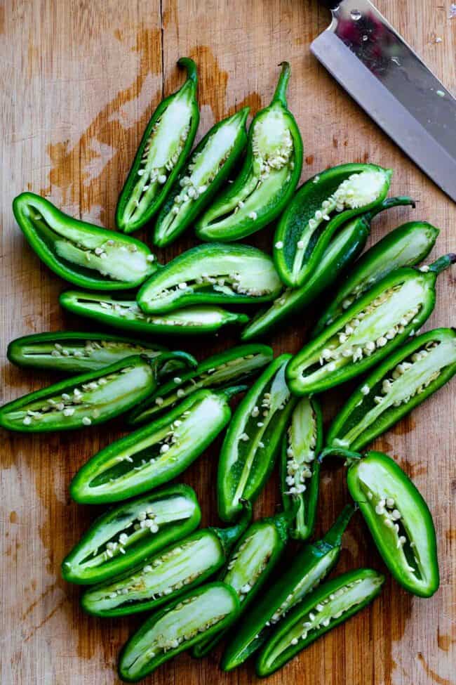 jalapenos sliced in half on a wooden cutting board.