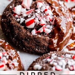 Close-up of chocolate peppermint cookies dipped in chocolate and topped with crushed peppermint candies, with a candy cane in the background. Text reads, Dipped Chocolate Peppermint Cookies.
