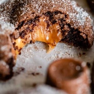 A close-up of gooey Rolo cookies with a caramel center, dusted with powdered sugar. The cookie is partially bitten, revealing melted caramel inside. Text overlay reads Homemade Gooey Rolo Cookies.