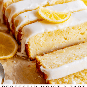 A sliced loaf of perfectly moist & tart glazed lemon bread topped with lemon slices sits on parchment paper, with fresh lemons in the background. The Food Charlatan.