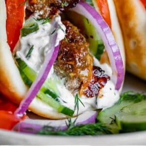A close-up of a Greek gyro filled with flavorful gyro meat, sliced red onions, tomatoes, cucumbers, and creamy tzatziki sauce in pita bread. The text reads: Restaurant Style Greek Gyros with Homemade Gyro Meat.