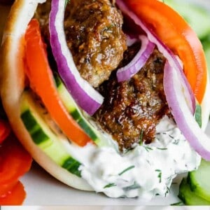 Close-up of a hand holding a Greek gyro filled with gyro meat, sliced tomatoes, cucumbers, red onions, and tzatziki sauce in pita bread. Text overlay reads, “Greek Gyros with Homemade Gyro Meat.”.