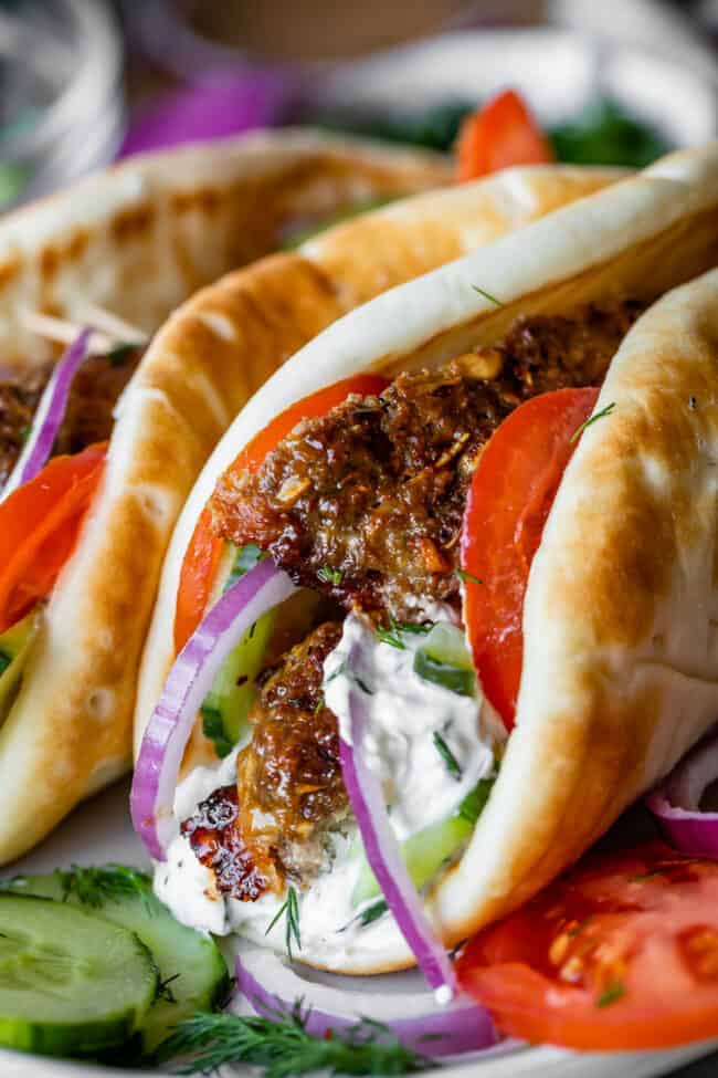 gyros with meat, tomatoes, tzatziki sauce, cucumbers, and red onion in pitas.