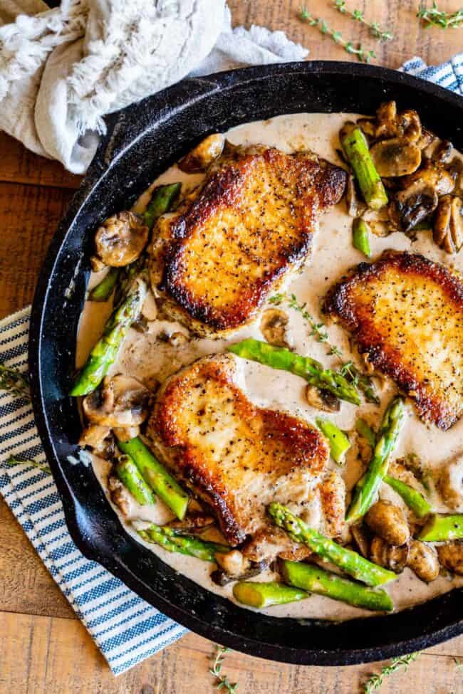 pork chops with asparagus, mushrooms, and a creamy pan sauce in a cast iron skillet.