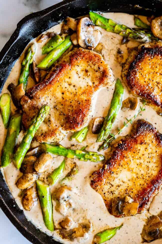 seared boneless pork chops with asparagus, mushrooms, fresh thyme, and creamy gravy in a cast iron skillet.