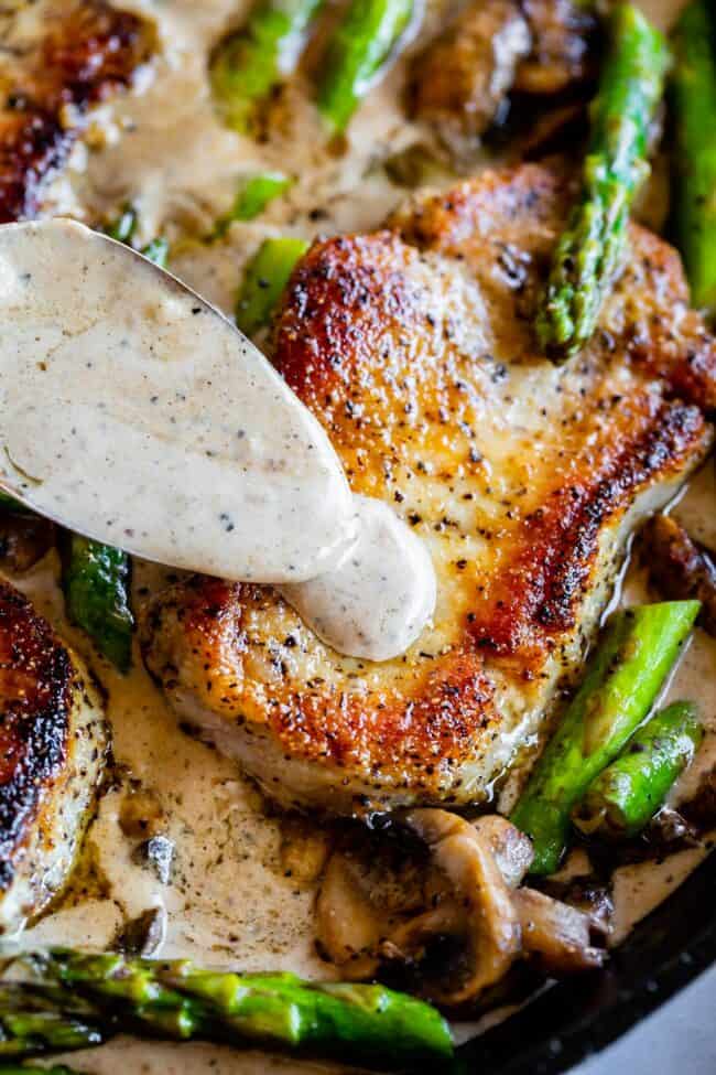 seared pork chops with asparagus, mushrooms, and a creamy gravy being spooned on top. 