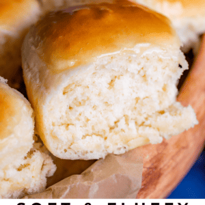 A close-up of golden-brown, soft dinner rolls in a wooden bowl, featuring a shiny, baked top and fluffy texture. Text at the bottom reads “Soft & Fluffy One Hour Dinner Rolls The Food Charlatan.”