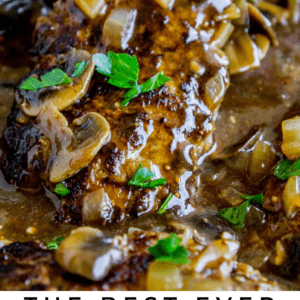 Close-up of Salisbury steak topped with mushroom and onion gravy in a skillet, garnished with fresh parsley. Text overlay reads: Salisbury Steak with Mushroom Gravy. The Food Charlatan.