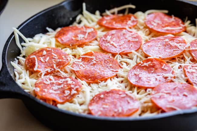 arranging pepperoni on top of a cast iron skillet pizza.