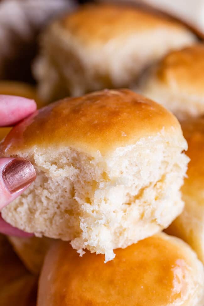 hand holding a homemade dinner roll with more rolls in the background.