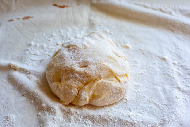 a ball of soft roll dough on a pastry cloth covered in flour.