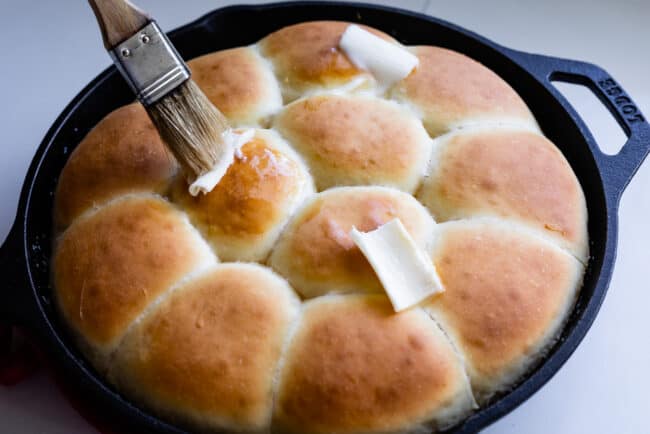 brushing butter on freshly baked rolls in a cast iron pan.