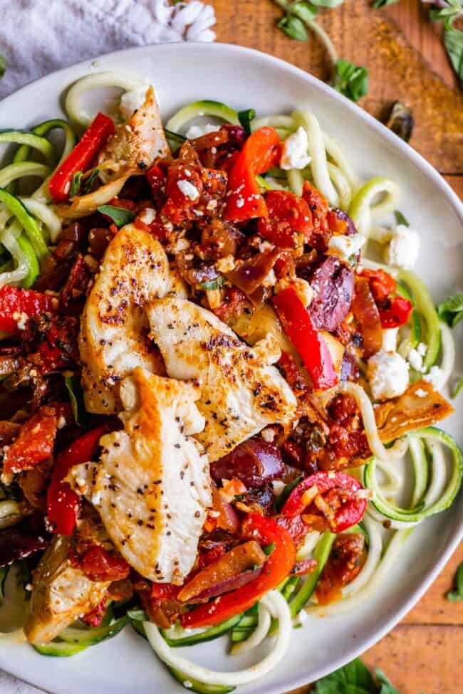 chicken, feta, and veggies over zucchini noodles on a white plate.