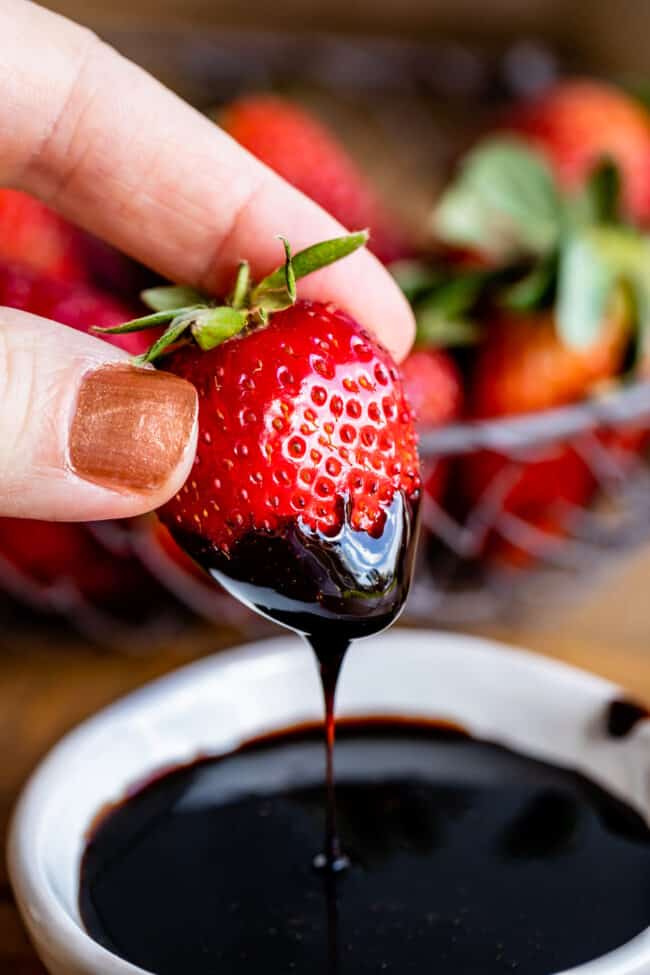 hand dipping a strawberry into balsamic vinegar reduction.