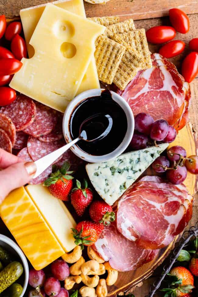 balsamic reduction glaze on a wooden charcuterie board with prosciutto, cheeses, crackers, fruits, nuts, and tomatoes. 