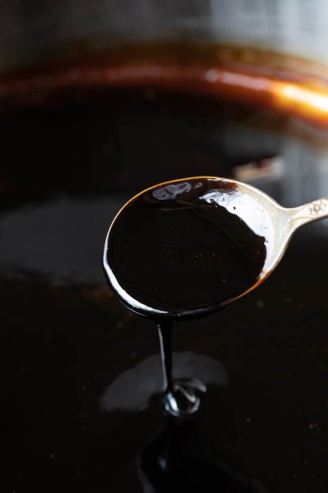 balsamic vinegar reduction pouring from a metal spoon back into the container.