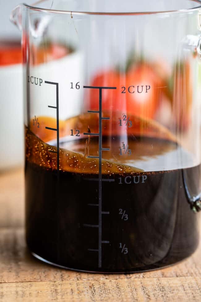 balsamic vinegar reduction glaze in a glass measuring cup with tomatoes in the background.