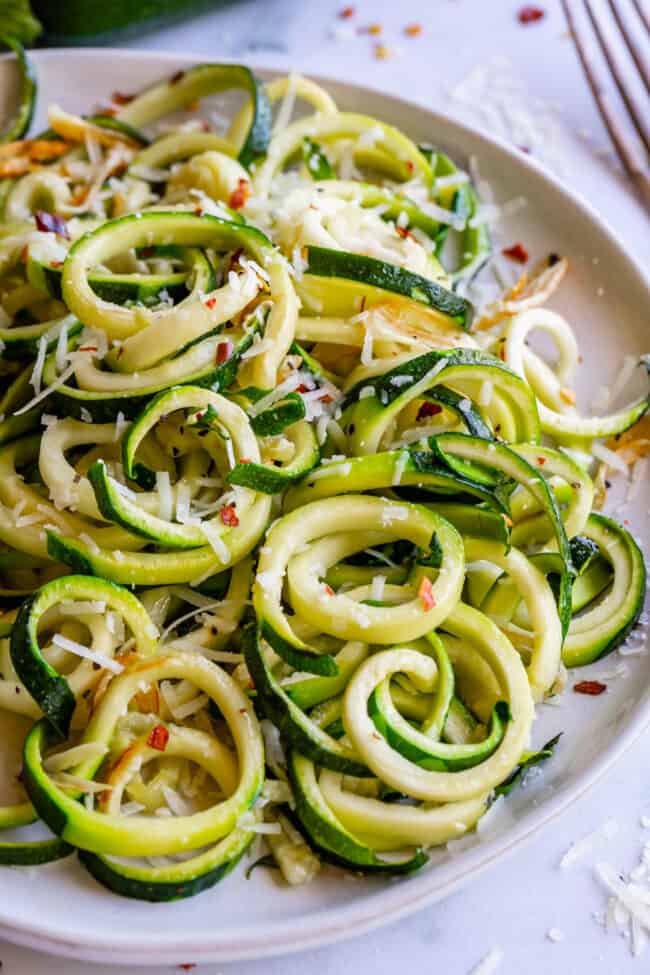 curly zoodles with parmesan and red pepper flakes on a white plate.