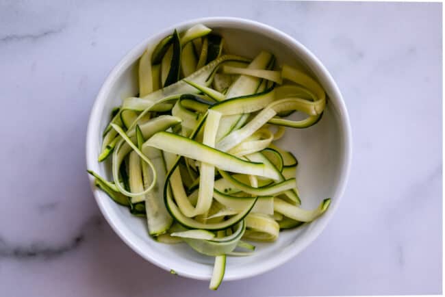 zucchini ribbons in a white bowl, made from a vegetable peeler