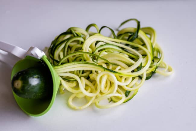 a zucchini being turned into zoodles using a handheld device