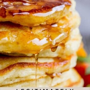 pin of stacked pancakes with bite sliced out and strawberries
