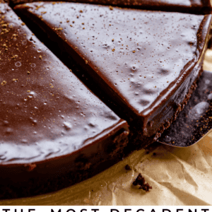 A rich, glossy flourless chocolate cake topped with chocolate ganache and a fresh strawberry. Text reads: The most decadent flourless chocolate cake with chocolate ganache. The Food Charlatan.