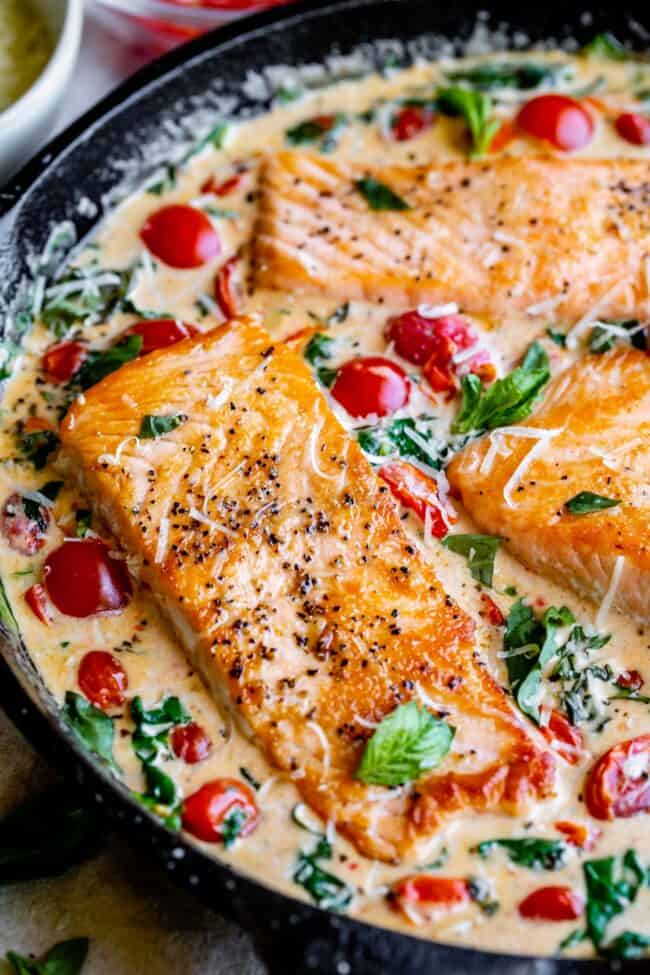 tuscan salmon in a skillet with cherry tomatoes, spinach, and basil.