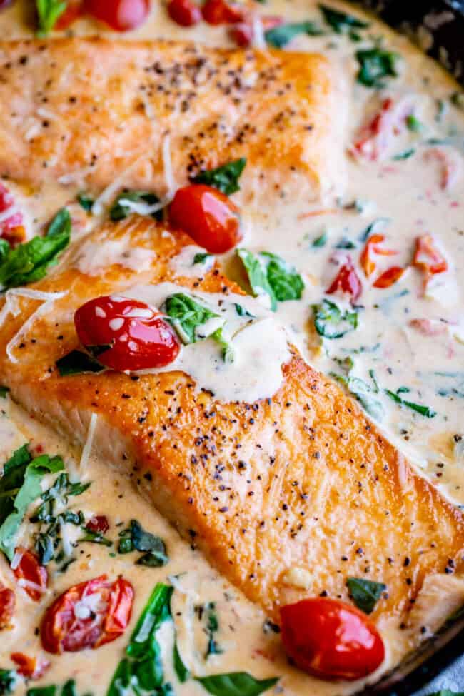 creamy tuscan salmon in a skillet with cream sauce, cherry tomatoes, fresh spinach, and fresh basil.