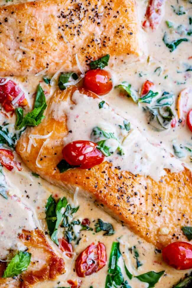closeup overhead shot of tuscan salmon with cream sauce, cherry tomatoes, spinach, and fresh basil. 