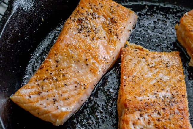 salmon with salt and pepper being seared in a skillet.