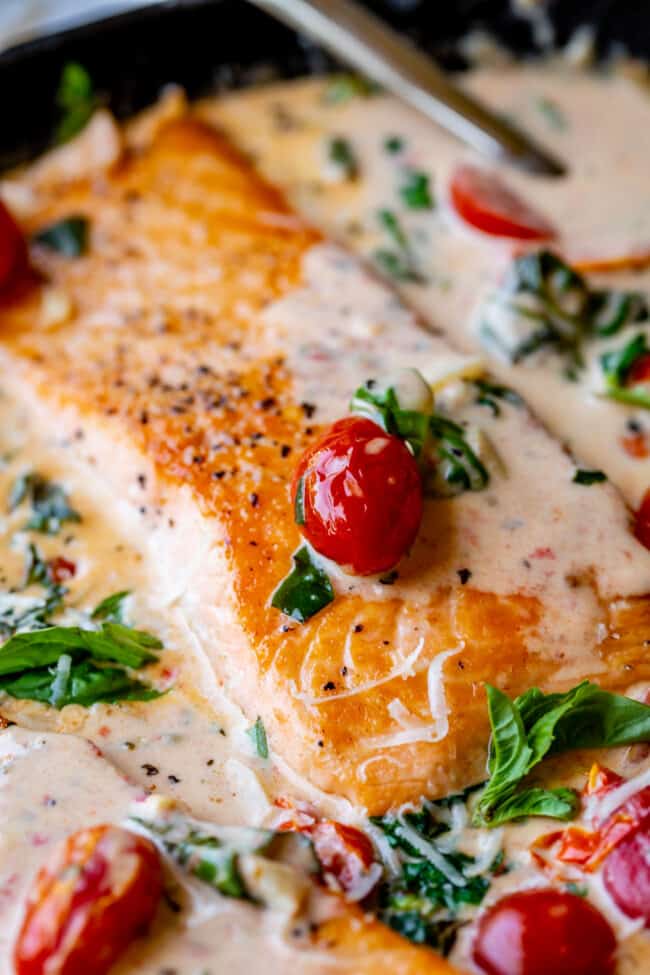 creamy garlic butter tuscan salmon closeup with cherry tomatoes, spinach, and fresh basil.