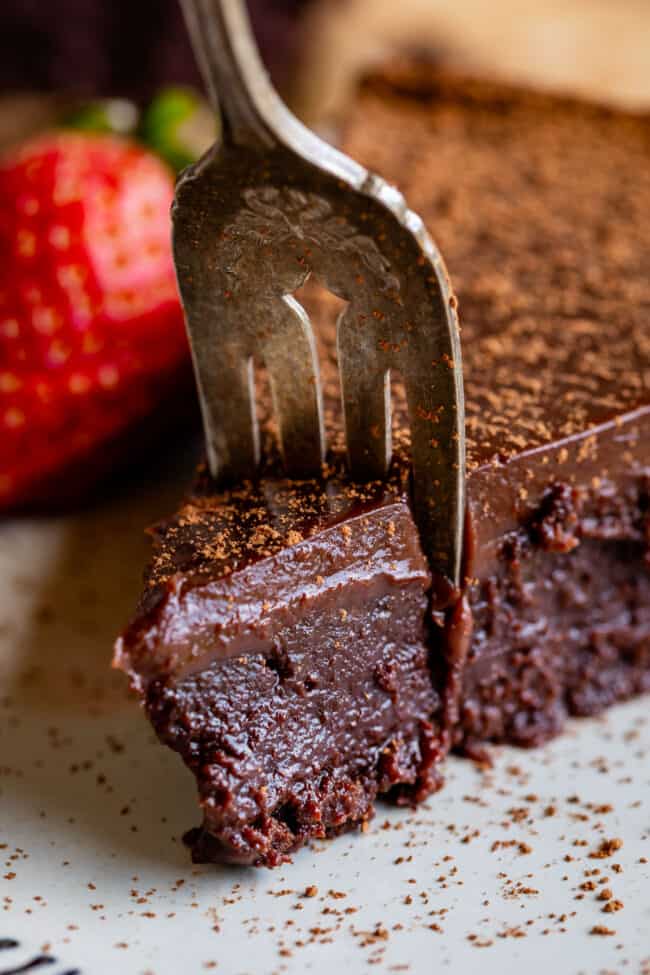 flourless chocolate cake with a fork in it next to a strawberry.