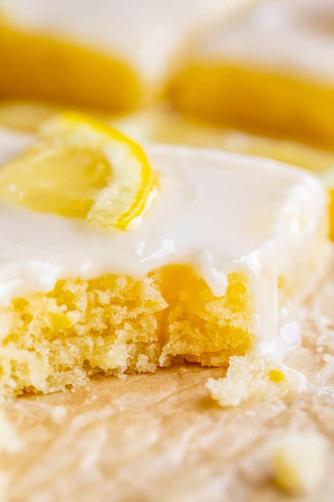 a piece of lemon sheet cake with glaze and a lemon slice with a bite taken out. 